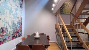 Un'area ristorazione moderna con un tavolo in legno, sedie e un quadro astratto dai colori vivaci appeso al muro.
