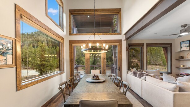 A spacious dining area with a long wooden table, surrounded by chairs, and a large window offering a view of a forested area. - Charming Ski Condo Near Keystone with Fireplace & Scenic Balcony (Keystone)