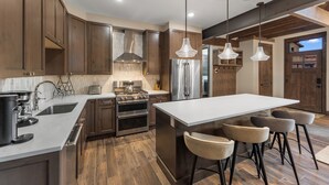A modern kitchen with wooden cabinets, stainless steel appliances, and a central island with bar stools. - Charming Ski Condo Near Keystone with Fireplace & Scenic Balcony (Keystone)