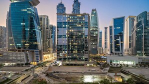 A modern cityscape with high-rise buildings, a central plaza with seating, and a construction site.