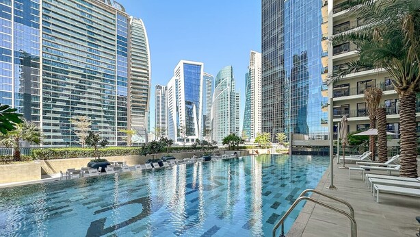 A swimming pool with a tiled deck, surrounded by high-rise buildings.