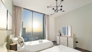 A hotel room with two beds, a large window with a city view, a modern chandelier, and a small bedside table with a vase.