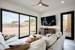A modern living room with a large TV, comfortable seating, and a view of the outdoors.
