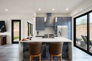 Una cocina moderna con una isla grande, gabinetes oscuros e iluminación colgante.