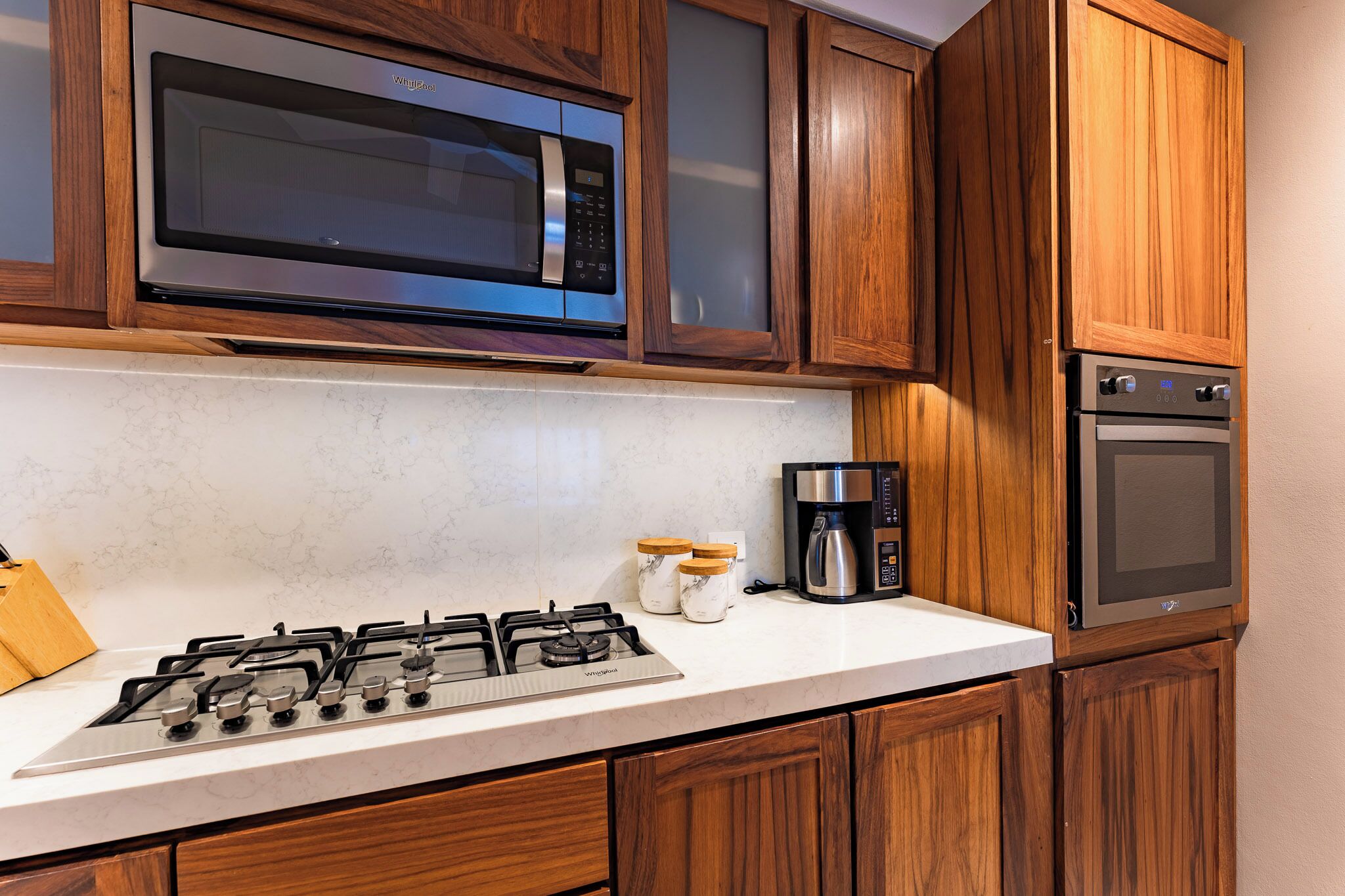 Una cucina con mobili in legno, un forno a microonde in acciaio inossidabile, un piano cottura a gas, una macchina da caffè e un forno integrato.