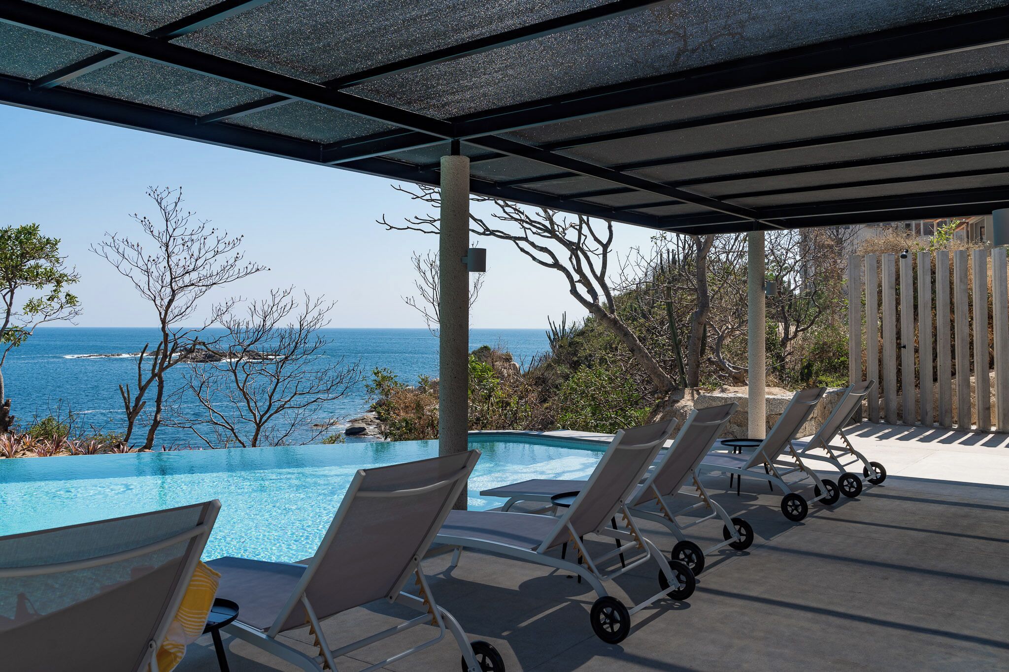 Une piscine à débordement avec des chaises longues et une vue sur l’océan.