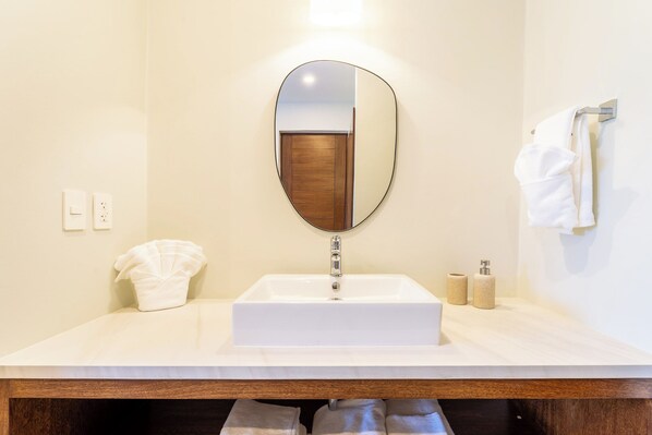 Un baño con un lavabo blanco, un espejo redondo, un perchero y dos botellas de jabón.
