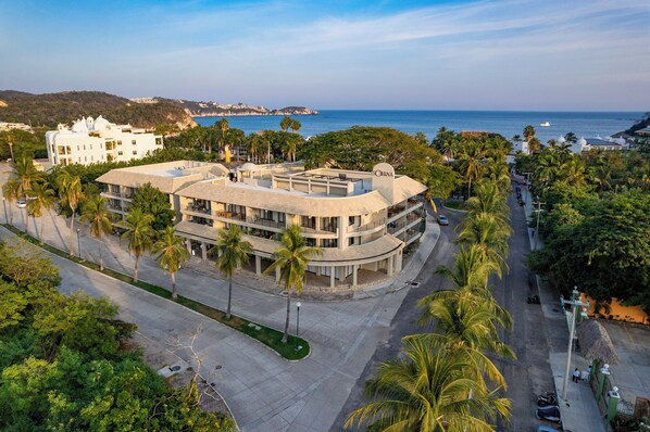 A modern hotel with a curved roof, surrounded by palm trees and a coastal view. - Short Walk to Beach & Town · 2nd Story · Solana (Huatulco)