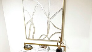 A console table with a gold frame, a decorative bowl, a book titled "Happiness Flower", and a gold ring.