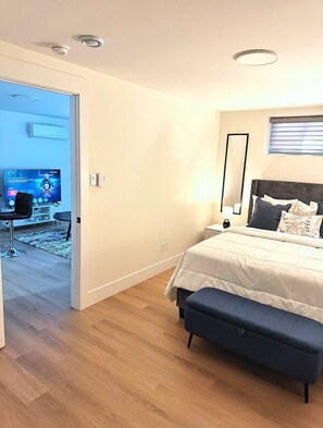 A modern bedroom with a bed, bedside table, and a TV in the adjacent room.