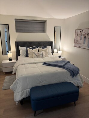 A bedroom with a bed, bedside tables, a bench, and a wall-mounted artwork.