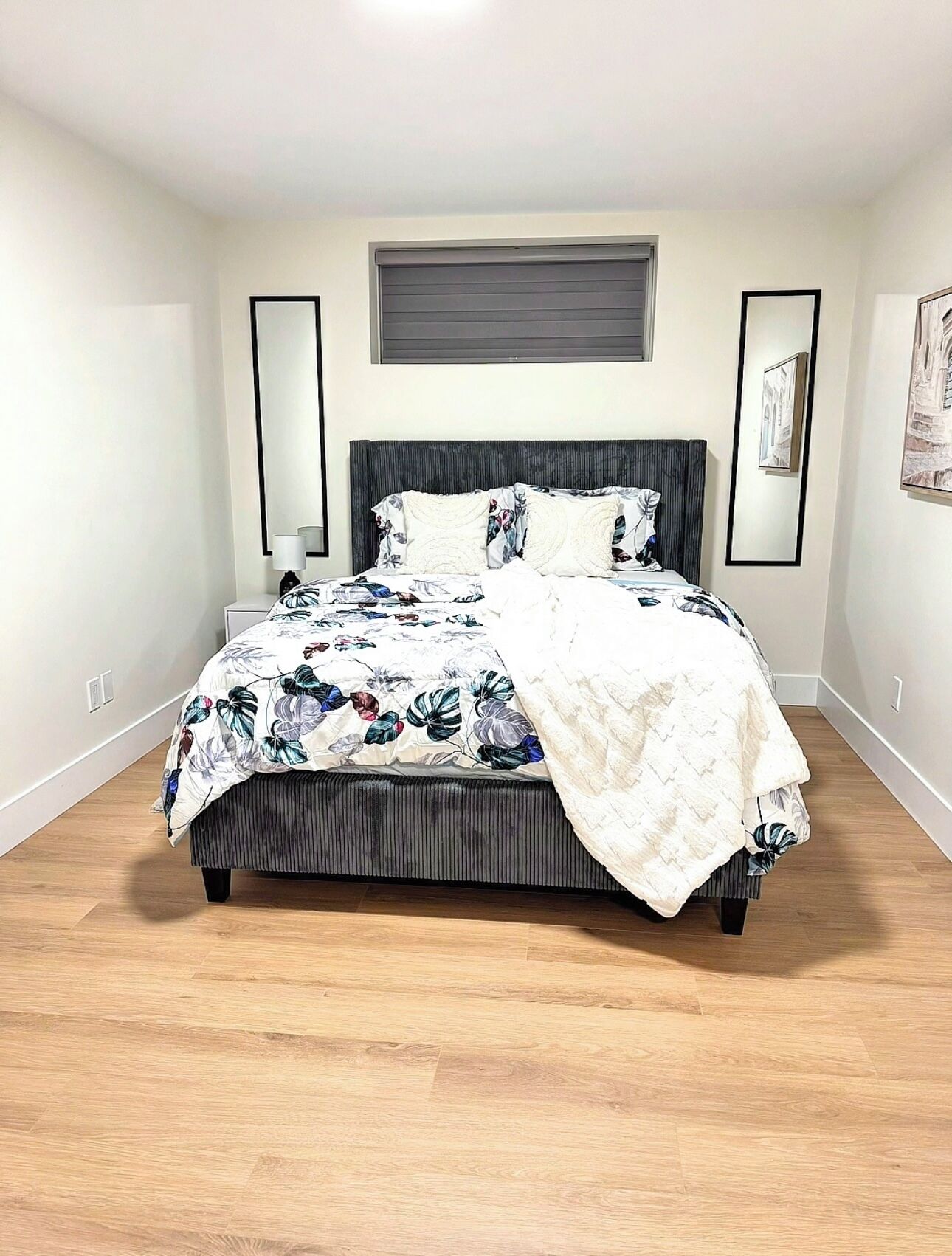 Una camera da letto con un letto, una testiera, una finestra e uno specchio fissato al muro.