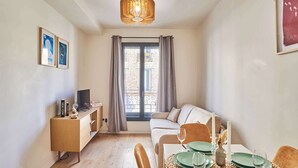 A modern living room with a sofa, dining table set for two, and a TV on a wooden stand.