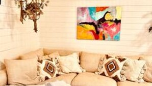 Un salon chaleureux avec un canapé beige, des coussins à motifs, une peinture abstraite aux couleurs vives et un luminaire tressé.