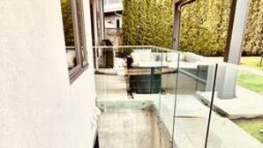 Un escalier moderne menant à un balcon en verre d’où l’on peut admirer un jardin.