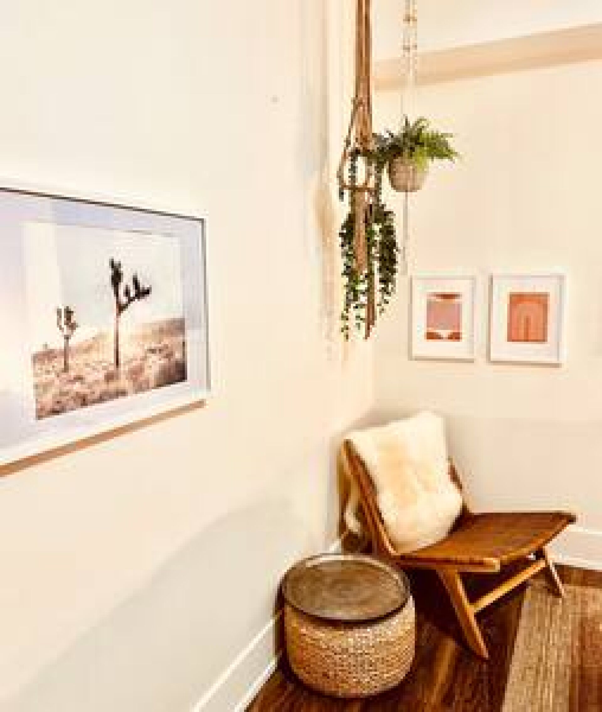 A room with a wooden floor, a cushioned chair, a round woven stool, and framed pictures on the wall.