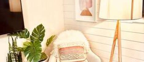 A cozy corner with a white armchair, a floor lamp, and a potted plant.