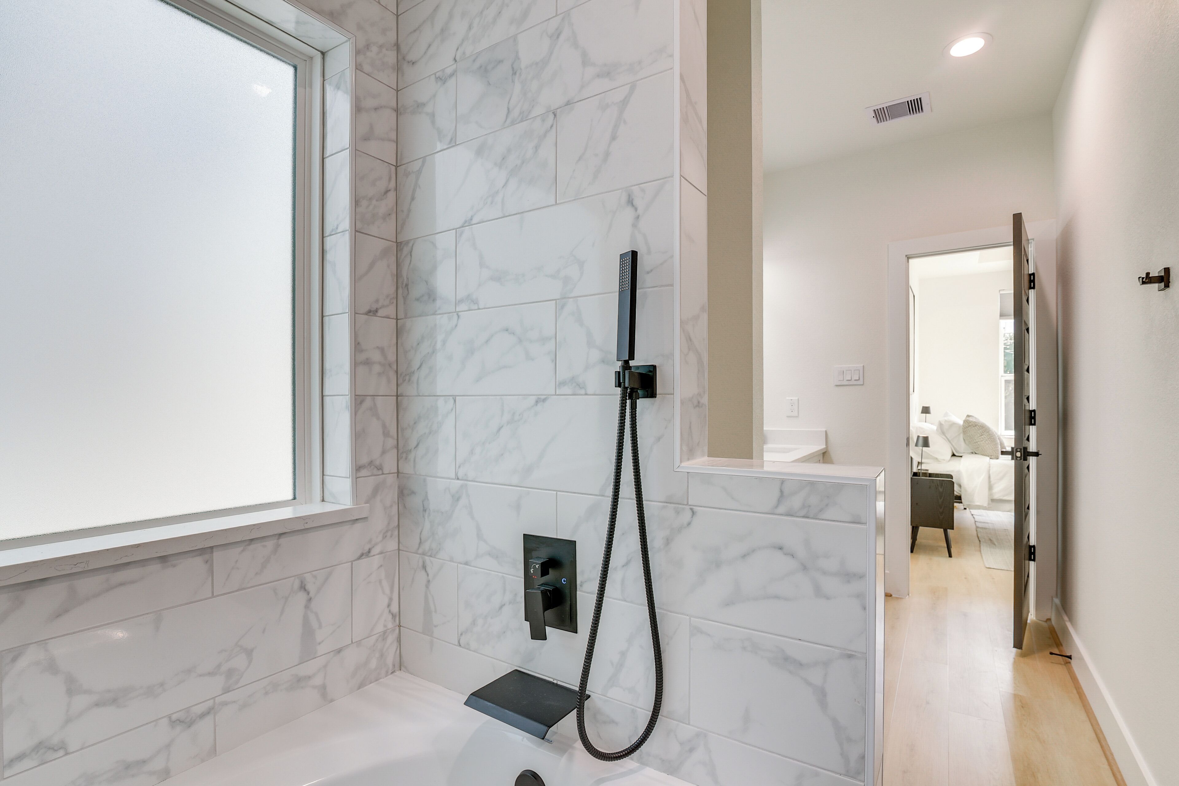A modern bathroom with a marble wall, a shower, and a window.