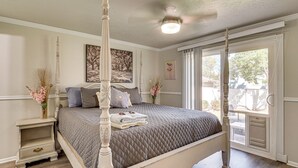 A four-poster bed with a quilted bedspread, a nightstand with a vase of flowers, and a large window with a view of the outdoors. - 2 Mi to Gardner Village: Family Gem w/ Fenced Yard (West Jordan)