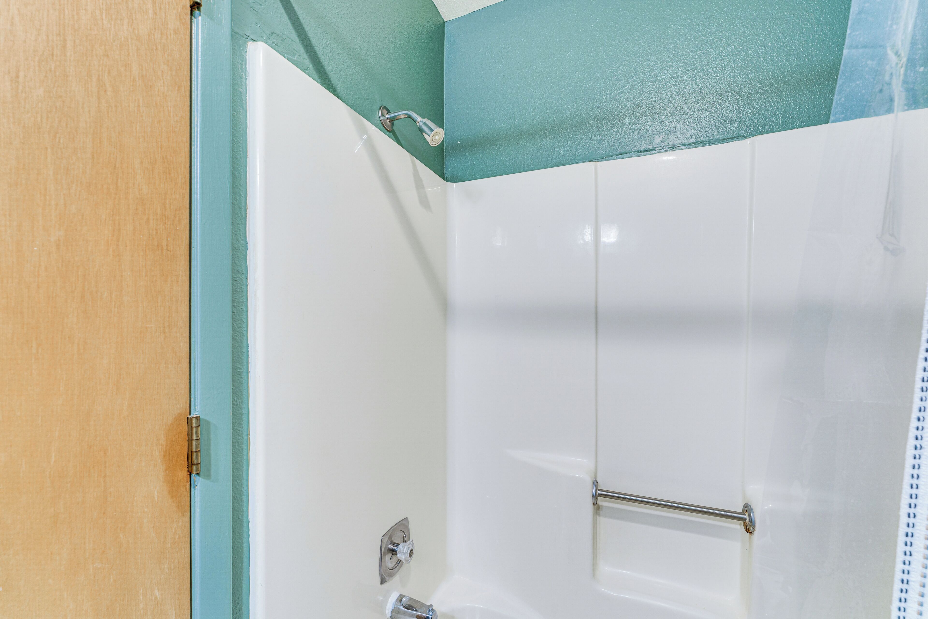 A corner of a bathroom with a white bathtub, a shower head, and a towel rack.