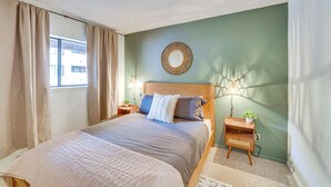 A bedroom with a bed, a bedside table with a lamp, a wall-mounted mirror, and a window with curtains. - Easy Red River Ski Access! Outdoor Adventure Condo (Red River)