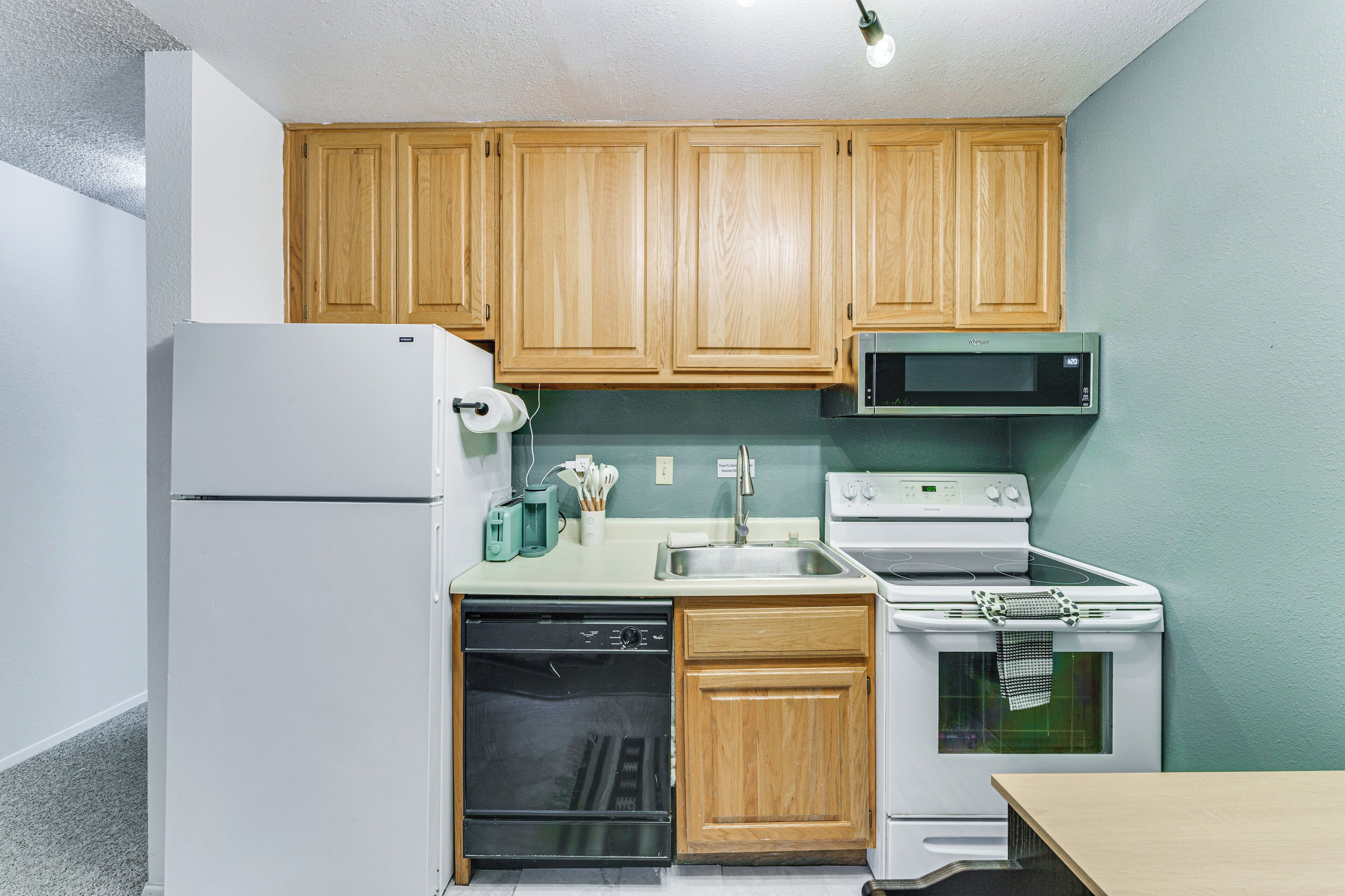 Une cuisine compacte avec des meubles en bois, un réfrigérateur blanc, un four à micro-ondes, une cuisinière et un lave-vaisselle.