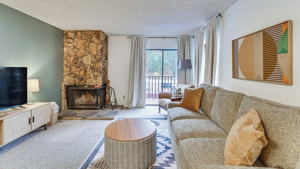 A living room with a stone fireplace, a sofa, a television, and a view of the outdoors. - Easy Red River Ski Access! Outdoor Adventure Condo (Red River)