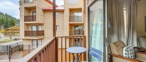A balcony with a wooden railing, a small round table, and a blue chair with a patterned cushion.