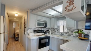 Une cuisine de taille réduite, avec des meubles blancs, un four à micro-ondes, une cuisinière et un évier.