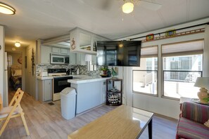 A compact kitchen with a microwave, stove, and sink, a dining area with a table, and a TV mounted above the counter. - 5 Mi to Surprise Stadium: Arizona Snowbird Getaway (Surprise)