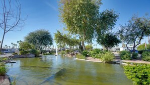 Un étang paisible avec une fontaine, entouré d’une végétation luxuriante et d’arbres.