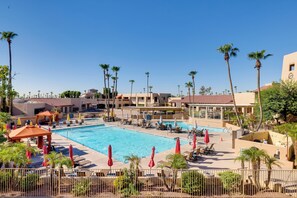 A large outdoor swimming pool with lounge chairs and umbrellas, surrounded by palm trees and hotel buildings. - 5 Mi to Surprise Stadium: Arizona Snowbird Getaway (Surprise)