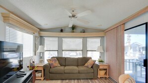 Ein Wohnzimmer mit einer Couch, zwei Beistelltischen, einem Deckenventilator und großen Fenstern mit Jalousien.