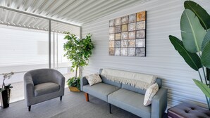 Ein modernes Wohnzimmer mit einem grauen Sessel, einem grauen Sofa mit weißer Decke, einer großen Pflanze und einem an der Wand hängenden Kunstwerk.