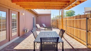 A covered patio with a wooden table and chairs, a sliding glass door, and a wooden fence. - 5 Mi to Dtwn: Tucson Townhome w/ Pool Access! (Tucson)