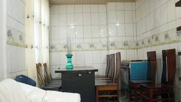 A compact kitchen with white tiled walls, a central island with a teal vase, wooden chairs, and a blue refrigerator.