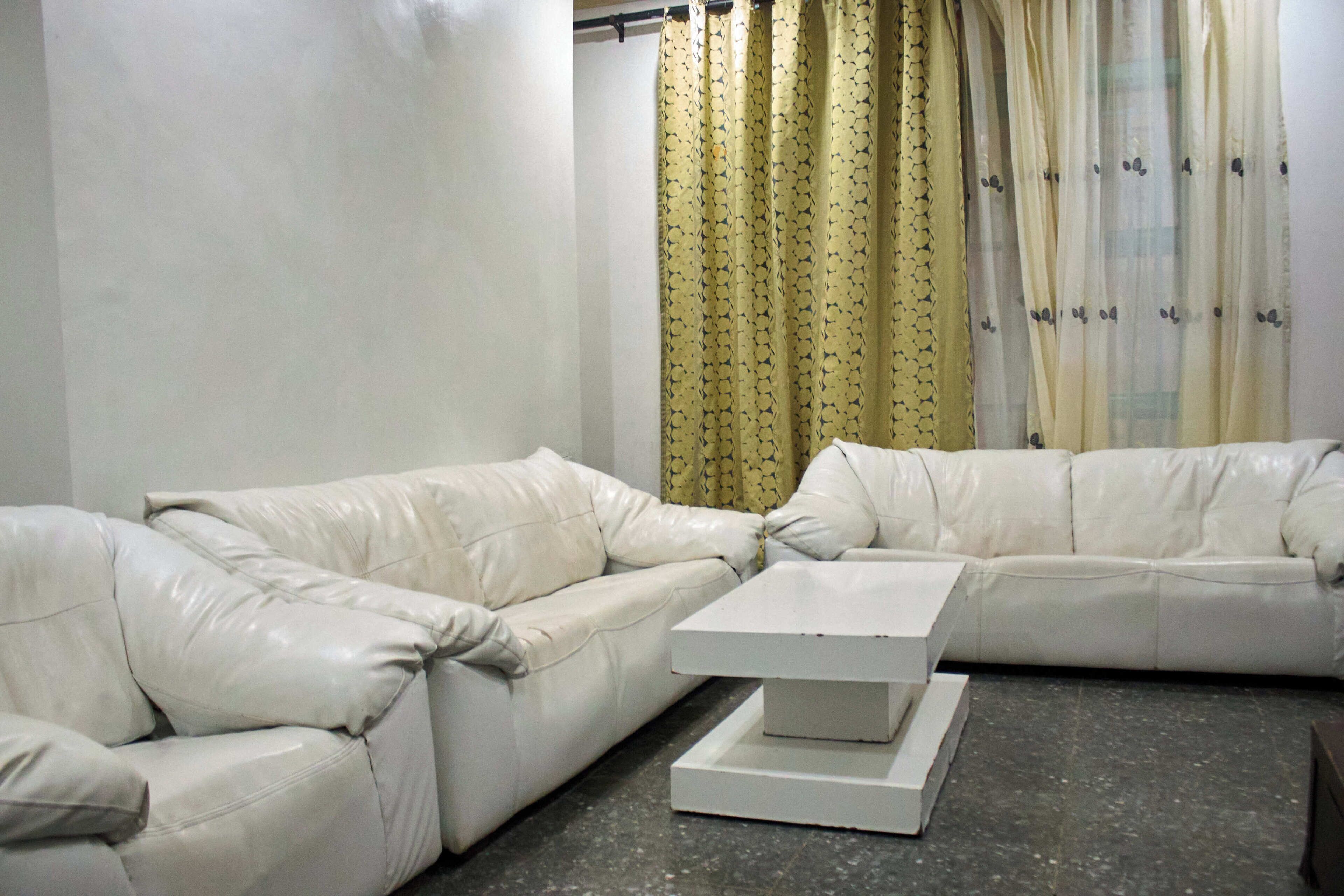 Una sala de estar con un sofá de cuero blanco, una mesa de centro blanca y una cortina con estampado de hojas.