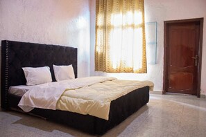 Una cama con cabecera oscura, almohadas blancas y una ventana con cortinas.