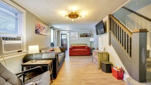 A spacious living area with a sofa, a coffee table, and a TV mounted on the wall. There is a staircase with a wooden railing leading to another level. - Little Woodland Home: Hidden Gem By Dtwn Bethlehem (Bethlehem)