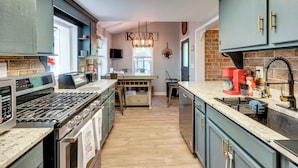 A modern kitchen with a central island, built-in appliances, and a brick accent wall. - Little Woodland Home: Hidden Gem By Dtwn Bethlehem (Bethlehem)