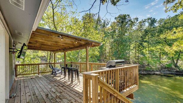 A wooden deck with outdoor seating and a grill, overlooking a river. - Lakefront Fun in Sunrise Beach! Pet-friendly Home! (Sunrise Beach)