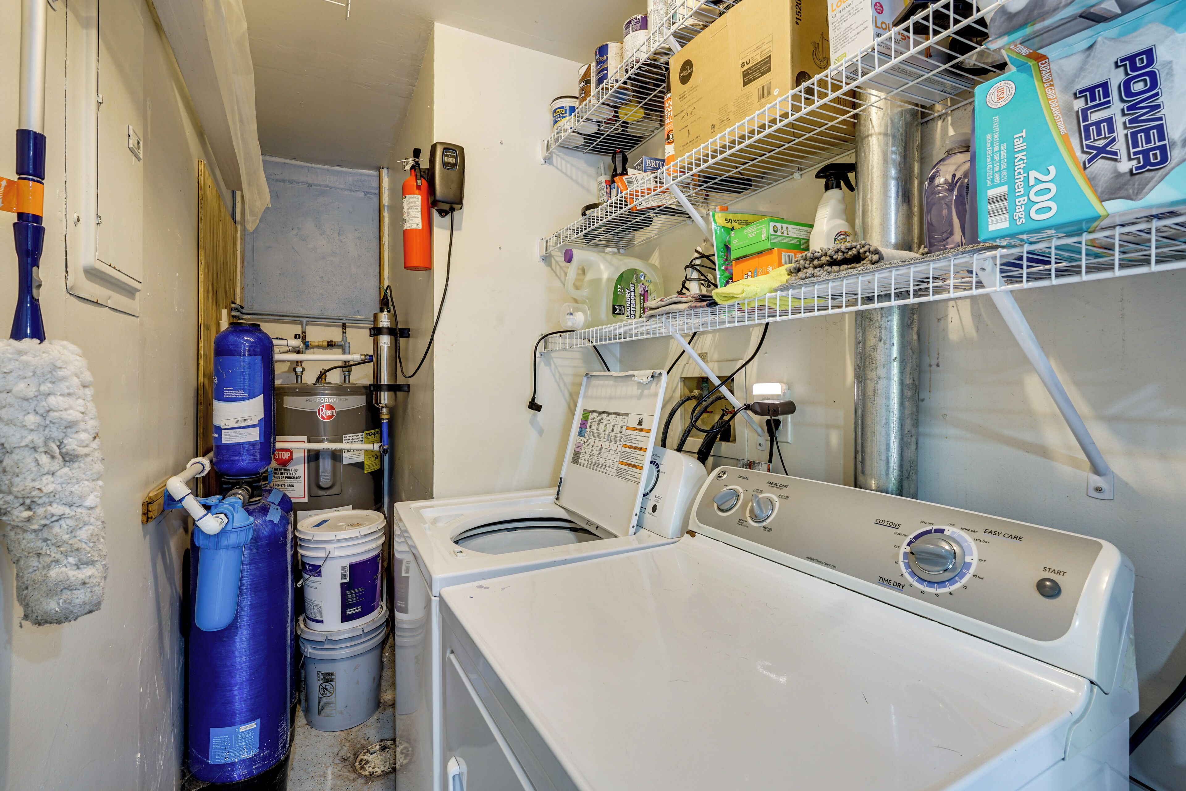 A laundry room with a front-loading washer and dryer, shelves with cleaning supplies, and a fire extinguisher.