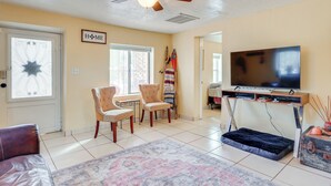 A living room with a ceiling fan, a television, two armchairs, a patterned rug, and a flag on the wall. - Walk Downtown: Authentic Adobe Home in Las Cruces! (Las Cruces)