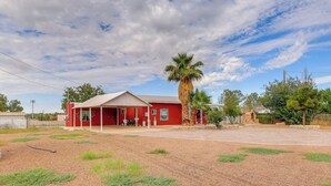 A red building with a covered porch, a palm tree, and a gravel driveway. - Walk Downtown: Authentic Adobe Home in Las Cruces! (Las Cruces)
