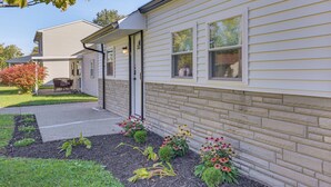 Einbungalow mit Eingangstür, einer kleinen Veranda und einem Garten mit verschiedenen Pflanzen und Blumen.