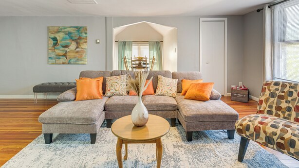 A living room with a sectional sofa, a patterned armchair, a vase on a side table, and a painting on the wall. - Walk to Coventry Village: Charming Top-floor Unit! (Cleveland Heights)