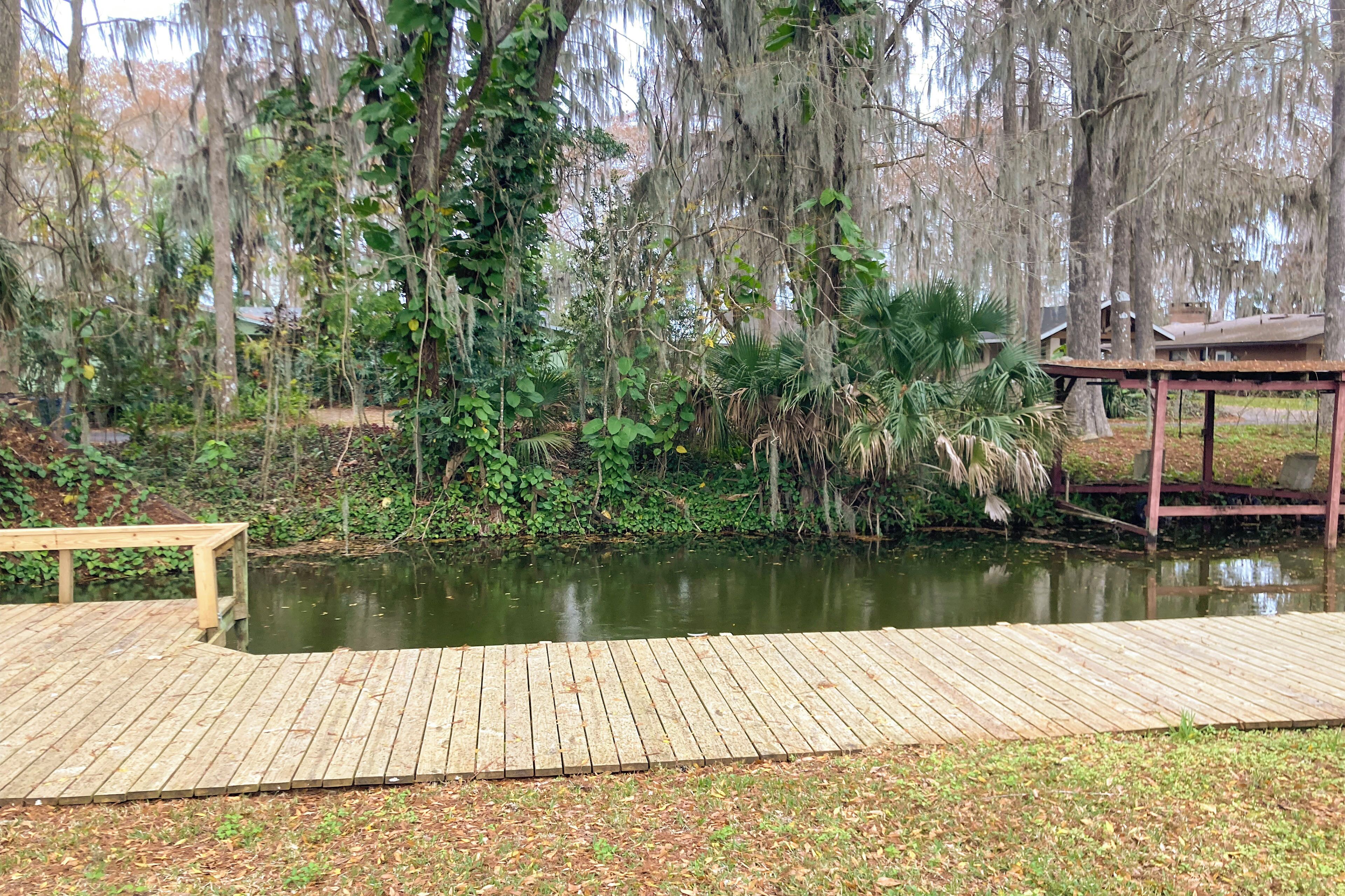 Un pont de fusta amb una banca, un estany i una glorieta en una zona boscosa.