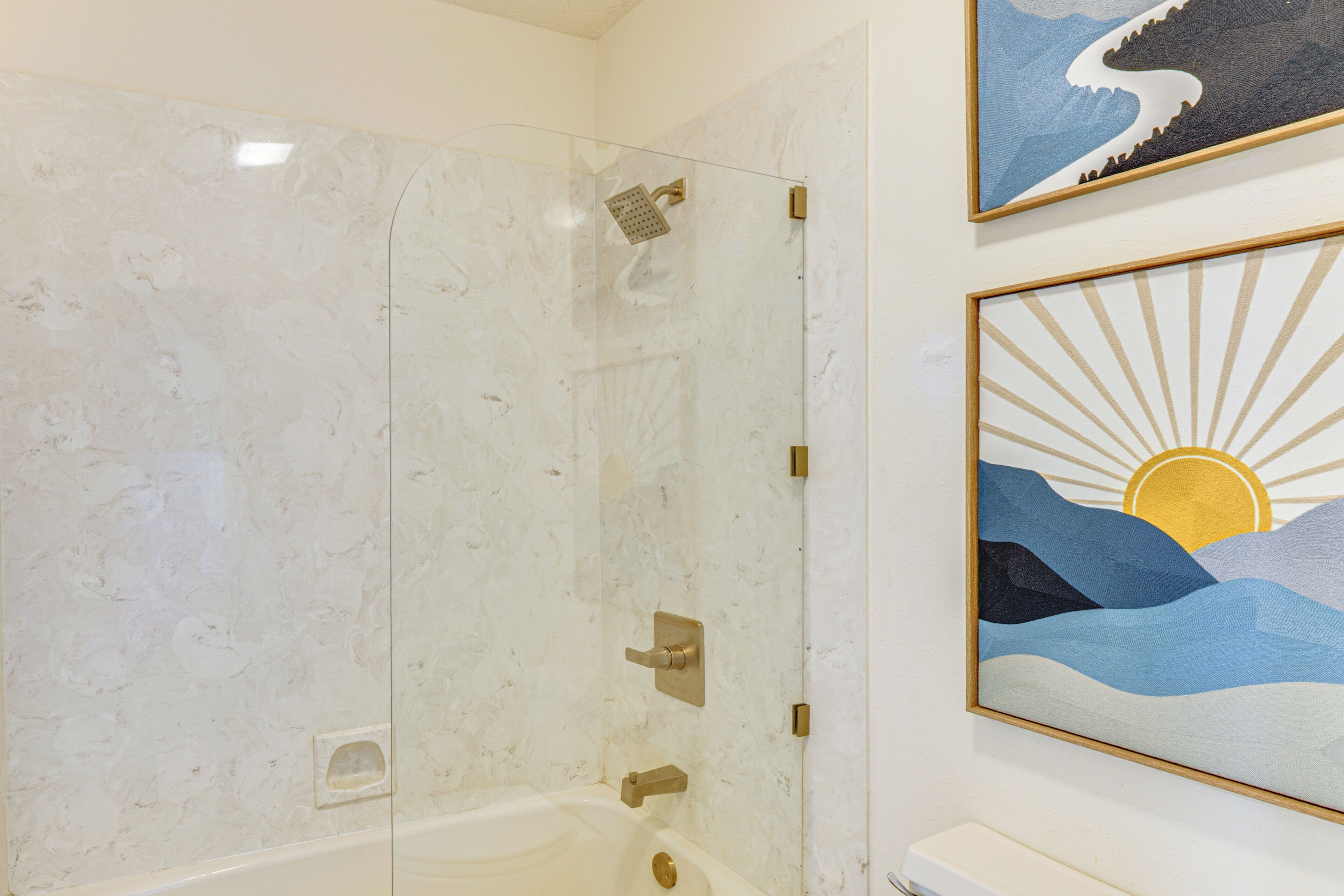 A bathroom with a glass-enclosed shower, a bathtub, and two framed artworks on the wall.