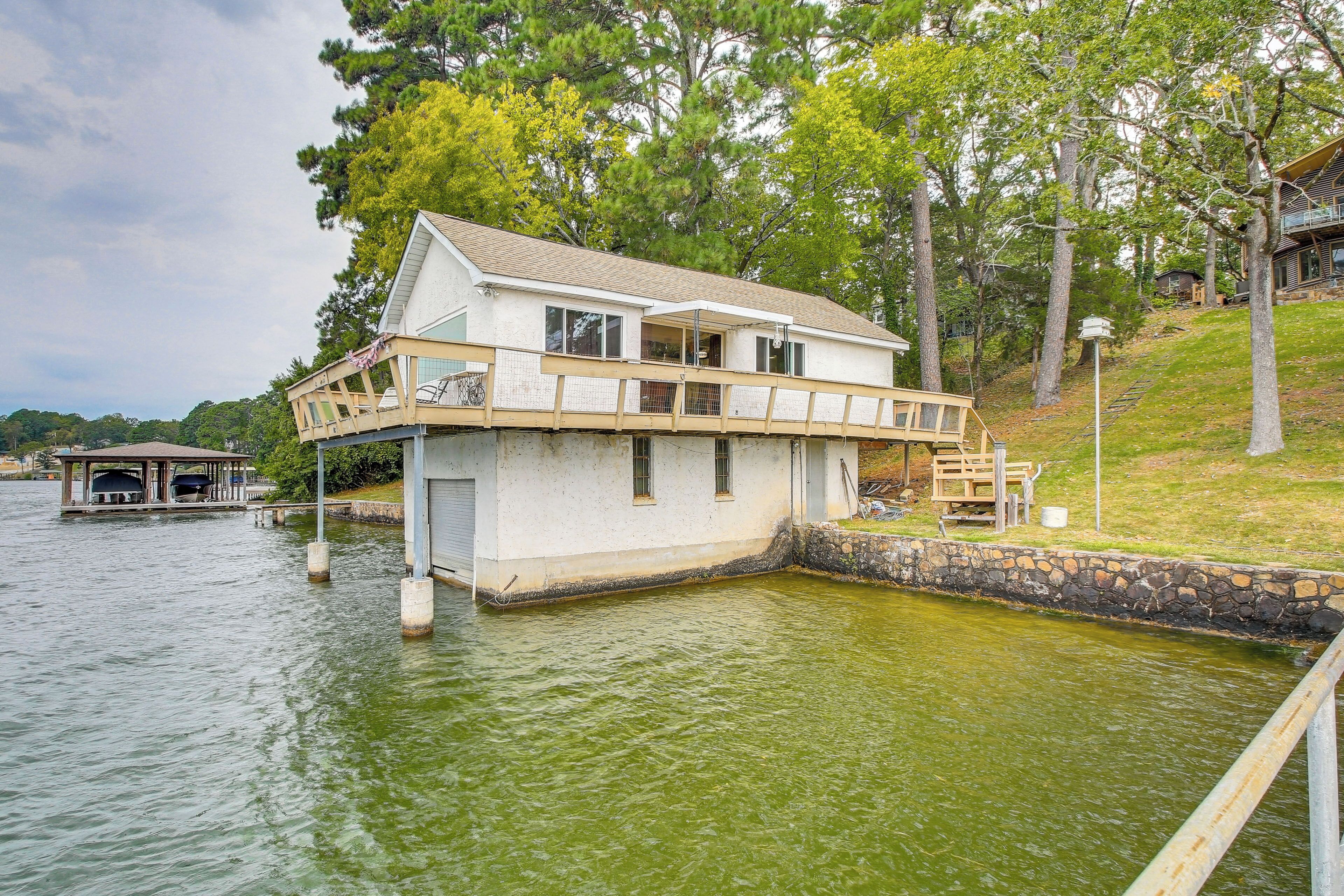 A houseboat with a balcony, situated on a body of water surrounded by trees.