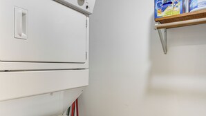Un espace buanderie aux murs blancs, avec un sèche-linge et une étagère au-dessus.